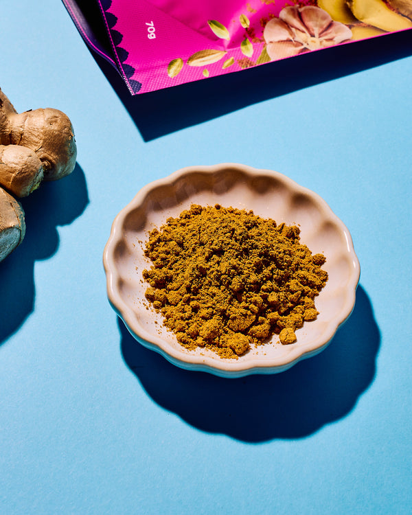 Turmeric powder in a bowl on a blue background with turmeric roots and a colorful package.